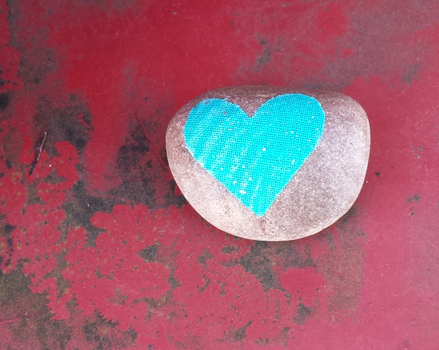 uncoated gray love-rock with aqua colored heart decoupage sitting on a red metal background with rust